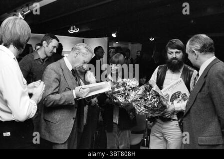 Präsentation des Buches "Ein Jahr in der Natur" in Amsterdam (Rosarium) Amsterdam Niederlande, Whizgle News, Dutch Desk, Niederlande, 1950 - 2000 am 04-11-1980. Das Bild enthält diese Themen. In einem lebhaften Innenbereich sorgt eine Zusammenkunft von mehreren Personen für eine lebendige Atmosphäre. Die Szene ist mit einer Mischung von Ausdrucksformen gefüllt, von fröhlichem Lächeln bis hin zu fokussiertem Look, die eine Mischung aus Emotionen zeigen. Im Vordergrund ist ein Gentleman, in einem hellen Anzug gekleidet, mit Schreiben beschäftigt, möglicherweise unterzeichnet er ein Buch. Er hat graue Haare und strahlt einen Hauch von Autorität oder Wichtigkeit aus. Neben ihm steht A Stockfoto