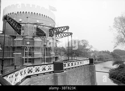 Cruquius im Bau Cruquius, Whizgle News, Dutch Desk, Niederlande, 1950 - 2000 am 16-10-1990. Diese Themen werden in der Abbildung angezeigt. Die Szene zeigt einen alten Turm mit einer runden Struktur, die deutlich hervorgehoben ist und eine Mischung aus Backstein und architektonischen Details zeigt. Die Krone des Turms ist mit Zinnen verziert, was ihm ein befestigtes Aussehen verleiht. Um den Turm herum befindet sich ein weitläufiges Gerüst, was darauf hinweist, dass die Restaurierungsarbeiten im Gange sind. Dies verleiht der Szene ein Gefühl von Aktivität und Zweck. Auf der linken Seite stehen die Gerüstststühle mit Holzbalken und Metallstützen, die sich durch Kontraste abheben Stockfoto