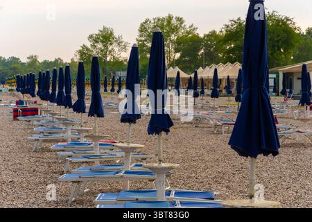 Kiesstrand mit leeren Reihen von Liegestühlen und Sonnenschirmen vor dem ruhigen Meer Stockfoto