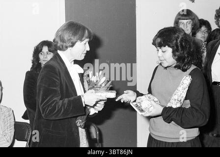 Film. Präsentation des Videos 'Türkische Kinder in Gastfamilien' Haarlem Kijkhuis Nederland, Whizgle News, Dutch Desk, Niederlande, 1950 - 2000 am 20-01-1984. Diese Themen sind in der Abbildung dargestellt. In einem gut beleuchteten Innenbereich stehen zwei Frauen einander gegenüber, um einen Moment des Austauschs zu erleben. Die Frau links trägt einen dunklen Samtblazer mit einer weißen Bluse darunter. Sie hat schulterlanges Haar und hält einen kleinen Blumenstrauß, der der Szene einen Hauch von Farbe und Lebendigkeit verleiht. Die Frau rechts, gekleidet in einem hellen, langärmeligen Oberteil, scheint Hand zu sein Stockfoto