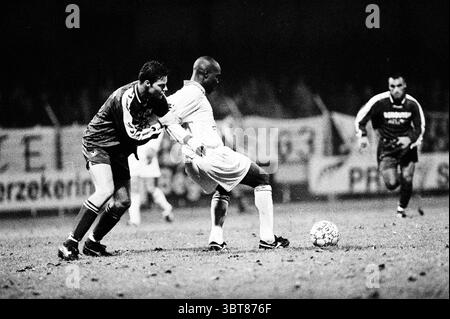 Telstar Football Match., Whizgle News, Dutch Desk, Niederlande, 1950 - 2000. Das Bild enthält diese Themen. Die Szene fängt einen intensiven Moment auf dem Spielfeld während eines nächtlichen Fußballspiels ein. Die Spieler sind in kontrastierenden Uniformen gekleidet; eine Mannschaft ist in tiefen Farben gehalten, während die andere in hellem weiß gehalten wird, was eine klare Unterscheidung zwischen den konkurrierenden Seiten ermöglicht. Im Vordergrund wird ein Spieler mit dunklem Gang in einen dynamischen Kampf um den Ball mit einem Gegner in weiß versetzt. Ihre Haltungen vermitteln Entschlossenheit und Leichtathletik, wobei sich der dunkle Spieler nach vorne lehnt und das weiß packt Stockfoto