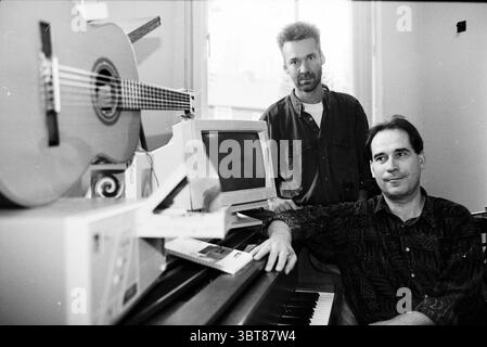 Art Aleman Paul Hofman IJmudien IJmuiden the Netherlands, Whizgle News, Dutch Desk, Niederlande, 1950 - 2000 am 08-10-1997. Diese Themen sind in der Abbildung dargestellt. In einem hellen Innenbereich befinden sich zwei Männer in einem gemütlichen Raum, der eine Atmosphäre der Kreativität und Zusammenarbeit vermittelt. Der erste Mann steht etwas links, mit einem kontemplativen Ausdruck. Er hat kurze, helle Haare und trägt ein dunkles, lässiges Hemd. Er lehnt sich an ein sichtbares Objekt, das wie eine hölzerne Gitarre aussieht, und deutet auf ein musikalisches Thema hin. Der zweite Mann sitzt rechts, mit mir Stockfoto