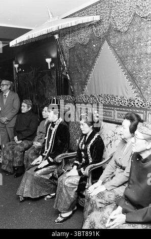 Indonesische Hochzeit im Restaurant Hilda am Wagenweg Hochzeitsrestaurant Haarlem Wagenweg Niederlande, Whizgle News, Dutch Desk, Niederlande, 1950 - 2000 am 09-03-1982. Dies sind die Elemente im Bild. In einem formellen Ambiente sitzt eine Gruppe elegant gekleideter Frauen auf aufwändig gestalteten Holzstühlen. Sie sind in traditioneller Kleidung mit satten Texturen und lebhaften Farben verziert. Tiefe Schwarz-, Gold- und andere Farbtöne bilden einen auffälligen Kontrast zum raffinierten Hintergrund. Die Frauen tragen ausgeklügelte Kopfbedeckungen und Schmuck, die ihr königliches Aussehen verstärken. Die Stockfoto