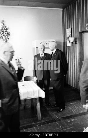 1. Stapel der neuen Fabrik. Größe Haarlem Paul Krugerkade The Netherlands, Whizgle News, Dutch Desk, Niederlande, 1950 - 2000 am 22-03-1961. Dies sind die Themen im Bild. In einem gut beleuchteten Innenraum mit Holzvertäfelung stehen zwei formale Figuren dicht beieinander und führen Gespräche. Beide sind in dunklen Anzügen und Krawatten gekleidet, was einen Hauch von Professionalität vermittelt. Ein Individuum ist etwas größer, mit weißem Haar, während das andere sich durch seinen Glatzkopf auszeichnet. Beide Ausdrücke vermitteln einen Moment aufmerksamen Dialogs. Im Hintergrund ein Coca-Cola-Automaten Stockfoto