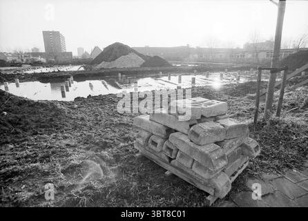 Boerhaavelaan Construction Site, Whizgle News, Dutch Desk, Niederlande, 1950 - 2000 am 22-11-1992. Diese Themen werden in der Abbildung angezeigt. Die Szene zeigt eine Baustelle, die von einer schroffen Landschaft geprägt ist, die überwiegend in Grautönen gehalten ist. Im Vordergrund wird ein Stapel schwerer, rechteckiger Betonblöcke ordentlich auf einer Holzpalette gestapelt. Ihre rauen Texturen stehen im Kontrast zu der umgebenden weichen Erde, die von verstreuten Grünflächen geprägt ist. Auf der linken Seite erhebt sich ein Erdhügel stark, dessen dunkle Konturen auf jüngste Ausgrabungen hindeuten. Der Boden ist unregelmäßig und mit Bereichen von bestreut Stockfoto