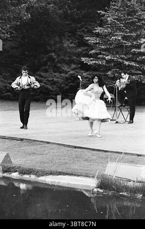 Spanische Tänze im Freien Bloemendaal Dancing Bloemendaal Hoge Duin en Daalseweg, Whizgle News, Dutch Desk, Niederlande, 1950 - 2000 am 19.06.1962. Diese Themen sind in der Abbildung dargestellt. Die Szene spielt im Freien, wahrscheinlich in einem Park oder Garten, geprägt von Grün und einer ruhigen Atmosphäre. Im Vordergrund treten zwei Tänzer auf einer Holzbühne auf. Eine Tänzerin trägt ein klassisches Schwarz-weiß-Outfit und zeigt lebhafte Fußarbeit, die Energie und Begeisterung ausstrahlt. Die andere Tänzerin, gekleidet in einem hellen, ausgestellten Kleid, wirbelt anmutig und schafft ein Gefühl von Bewegung und Eleganz. Ihr Kleid f Stockfoto