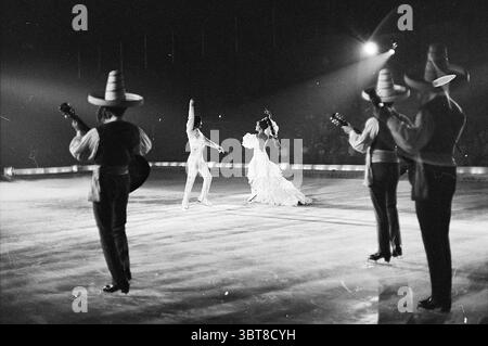 Wiener Ice Revue Show, Whizgle News, Dutch Desk, Niederlande, 1950 - 2000 am 05-08-1969. Diese Themen sind in der Abbildung dargestellt. Die Szene fängt eine lebendige Vorstellung auf einer geräumigen Bühne ein, auf der ein Paar elegant im Zentrum tanzt. Die Tänzerinnen tragen auffällige Kostüme; die Frau trägt ein fließendes weißes Kleid mit komplizierten Rüschen, die sich anmutig mit ihr bewegen, während sie sich dreht, während der Mann in ein leichtes, möglicherweise weißes Outfit gekleidet ist, das ihre Kleidung ergänzt. Um die Tänzer herum steht in einem Halbkreis ein kleines Ensemble von Musikern, die jeweils traditionelle Instrumente spielen Stockfoto