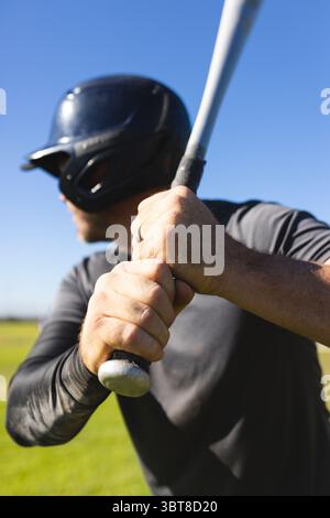 Männlicher Athlet, der Baseballschläger über die Schulter auf dem Feld mit Helm und zeigendem Ring greift Stockfoto