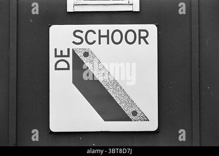 Bericht Naco Hoorn Naco Report, Whizgle News, Dutch Desk, Niederlande, 1950 - 2000 am 03-08-1967. Diese Themen werden in der Abbildung angezeigt. Die Szene zeigt ein quadratisches Schild, das gut sichtbar an einer dunklen Wand angebracht ist, wahrscheinlich aus Metall oder lackiertem Holz. Der Hintergrund ist ein einheitlicher, gedämpfter Farbton, der im Kontrast zum Zeichen selbst steht. Das Schild selbst ist hauptsächlich weiß und enthält eine stilisierte Grafik, die eine schräge Form oder ein Rechteck darstellt. Diese Form ist mit einem Muster gefüllt, das auf eine Textur hinweist und möglicherweise das Erscheinungsbild einer Oberfläche wie Stein oder Beton imitiert. Das Schild ist fett, bl Stockfoto