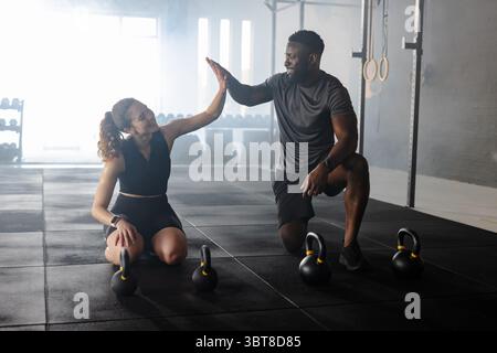 Verschiedene Trainingspartner heben Kettlebells im Fitnessstudio mit Fitness-Tracker unter Ringen Stockfoto