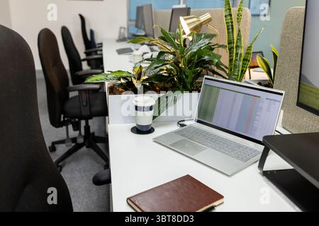 Der silberne Laptop mit Tabellenkalkulationstabelle sitzt mit Kaffeetasse, Lampe und Pflanzen auf dem Schreibtisch im Büro Stockfoto