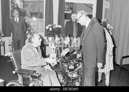 Installation von Bürgermeister Machielsen Zandvoort Mayors, Whizgle News, Dutch Desk, Niederlande, 1950 - 2000 am 05-10-1977. Dies sind die Elemente im Bild. Die Szene zeigt ein formelles Treffen, wahrscheinlich ein Ereignis, bei dem ein Meilenstein oder eine Anerkennung gefeiert wird. Im Vordergrund schütteln zwei Personen im Rollstuhl einen Handschlag. Eine Person mit Brille und hellem Pullover drückt ein warmes Verhalten aus, während die andere, in dunklerer Kleidung gekleidet, empfänglich erscheint. Hinter ihnen beobachten mehrere Figuren die Interaktion. Diese Individuen sind in formeller Kleidung gekleidet, mit unterschiedlichen Stilen, Suggestion Stockfoto
