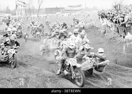Motocross Wijchen Sidecar Motorcycles Motorcycle Race, Whizgle News, Dutch Desk, Niederlande, 1950 - 2000 am 20-03-1978. Dies sind die Elemente im Bild. Die Szene zeigt ein pulsierendes Motocross-Rennen, das sich auf einer schroffen Feldstrecke voller Staub und Spannung abspielt. Im Vordergrund stehen Motorräder und Beiwagen, die mit unterschiedlichen Designs und leuchtenden Farbtupfern wie Rot, Blau und Gelb ausgestattet sind. Die in Schutzkleidung gekleideten Fahrer strahlen eine Mischung aus Entschlossenheit und Nervenkitzel aus, wobei ihre Helme das Umgebungslicht reflektieren. Im Hintergrund wird eine Masse von sp Stockfoto