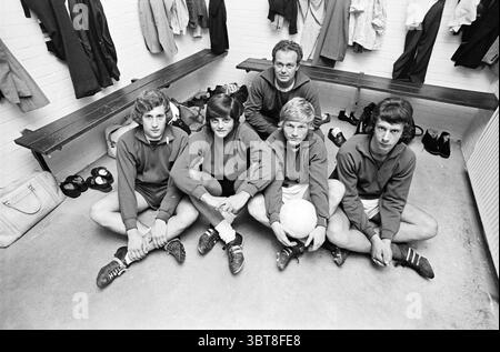 Spieler Zandvoort Meeuwen Football Zandvoortse Meeuwen Halfweg, Whizgle News, Dutch Desk, Niederlande, 1950 - 2000 am 02-09-1971. Dies sind die Elemente im Bild. In einem geräumigen Umkleideraum sitzen fünf junge Männer eng zusammen auf dem Boden, in einer entspannten Position. Sie tragen dazu passende sportliche Oberteile in dunklen Farben und leichte Shorts, die auf Teamgeist hinweisen. Ihre Schuhe, die deutlich sichtbar sind, sind mit markanten Fußballschuhen ausgestattet. Der Hintergrund zeigt Holzbänke, die an weißen Ziegelwänden gesäumt sind und eine einfache, aber funktionale Atmosphäre schaffen. Verschiedene Elemente, einschließlich Stockfoto