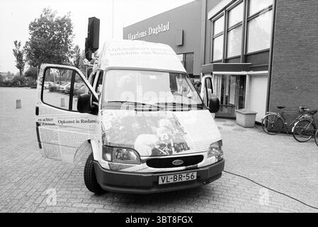 Neuer Werbebus HD Haarlem the Netherlands, Whizgle News, Dutch Desk, Niederlande, 1950 - 2000 am 29-07-1996. Das Bild enthält diese Themen. Die Szene zeigt einen Van, der durch sein einzigartiges Äußere besticht, das mit großen Zeitungsausschnitten bedeckt ist, was ihm ein markantes und unkonventionelles Aussehen verleiht. Die Türen des Fahrzeugs sind weit geöffnet, was zur Neugier einlädt und den Innenraum teilweise sichtbar macht. Der Van selbst hat aufgrund des Schwarz-weiß-Designs des Zeitungsdrucks ein überwiegend graues und weißes Farbschema. Die Umgebung des Fahrzeugs zeichnet sich durch eine moderne, urbane Umgebung aus Stockfoto