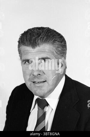 Porträt eines Mannes ca. 50 Jahre alt im Kostüm, Whizgle News, Dutch Desk, Niederlande, 1950 - 2000 am 08-08-1978. Das Bild enthält diese Themen. In der Szene sitzt ein Mann mittleren Alters vor einem einfachen, hellen Hintergrund, der seine Eigenschaften betont. Sein Haar ist dick, wellig gestylt und zeigt eine Mischung aus dunklen und grauen Tönen, die zu seinem eleganten Aussehen beitragen. Der Mann trägt eine gut geschnittene, dunkle Anzugsjacke über einem hellen Hemd, ergänzt durch eine gestreifte Krawatte mit einer Kombination aus dezenten Farben, die einen dynamischen und professionellen Look kreieren. Sein Expressi Stockfoto
