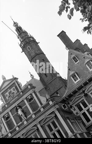 Turm des Rathauses in Haarlem Haarlem Grote Markt Niederlande, Whizgle News, Dutch Desk, Niederlande, 1950 - 2000 auf 31-10-1991. Dies sind die Elemente im Bild. Die Szene zeigt ein beeindruckendes Gebäude, das durch komplexe architektonische Details gekennzeichnet ist. Die Struktur wird aus einem niedrigen Winkel erfasst, was ihre Höhe und Pracht unterstreicht. Auf der linken Seite steht ein hoher Turm, der von einem Turm gekrönt ist, der in Richtung Himmel reicht. Die Oberfläche des Turms zeigt ein verwittertes Aussehen, was auf Alter und Geschichte hindeutet, wobei mehrere kleine Fenster entlang der Höhe sichtbar sind. Das Gebäude selbst ist es Stockfoto