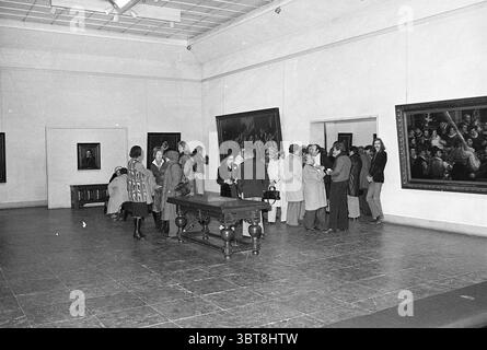 Reiseveranstalter im Frans Hals Museum Frans Hals Museum, Whizgle News, Dutch Desk, Niederlande, 1950 - 2000 am 19-01-1977. Dies sind die Themen im Bild. In einer geräumigen Kunstgalerie ist die Szene voll von Gruppen von Menschen, die sich mit Gesprächen beschäftigen und die Kunstwerke schätzen, die die Wände säumen. Die Umgebung hat ein anspruchsvolles Ambiente, gekennzeichnet durch hohe Decken und ein minimalistisches Design, mit weißen Wänden, die die Gemälde hervorstechen lassen. Der Boden besteht aus dunklen, polierten Fliesen, die ein Gefühl von Eleganz verleihen. Große, gerahmte Kunstwerke dominieren die Wände, von Porträts bis hin zu Stockfoto