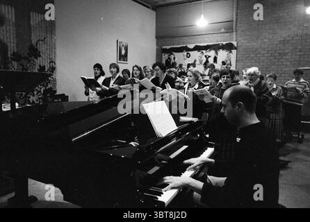 Probe H.C.O.V. in der Petra-Kirche IJmuiden Spaarnestraat Niederlande, Whizgle News, Dutch Desk, Niederlande, 1950 - 2000 am 13-03-1996. Diese Themen sind in der Abbildung dargestellt. In einem gemütlichen Innenbereich steht eine Gruppe von Menschen in organisierter Formation und nimmt an einer Chorvorstellung Teil. Sie halten jeweils Notenblätter, deren Ausdruck Konzentration und Begeisterung widerspiegelt. Die Individuen sind in einer Mischung aus formeller und lässiger Kleidung gekleidet, was auf eine Gemeindeversammlung oder eine Probe hindeutet. An der Spitze spielt ein Mann einen Flügel, mit den Fingern über den Tasten. Er konzentriert sich auf das M Stockfoto