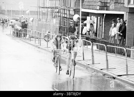 Beenden Sie North Holland Cycling Champion Cycling, Whizgle News, Dutch Desk, Niederlande, 1950 - 2000 am 23-05-1981. Die Abbildung zeigt diese Themen. Die Szene fängt einen dynamischen Moment bei einem Radrennen auf einer regendurchfluteten Straße ein. Zwei Radfahrer dominieren den Vorderboden, ihre Körper sind nach vorne geneigt, während sie intensiv in die Pedale treten, die Muskeln sind gespannt. Der Radfahrer auf der linken Seite trägt einen dunklen Helm und ein ärmelloses Oberteil mit kontrastfarbenen Shorts, während die rechte mit einem hellen Trikot bekleidet ist. Beide zeigen leuchtende Farben, die sich von den monochromen Tönen des nassen Asphalts abheben. Stockfoto