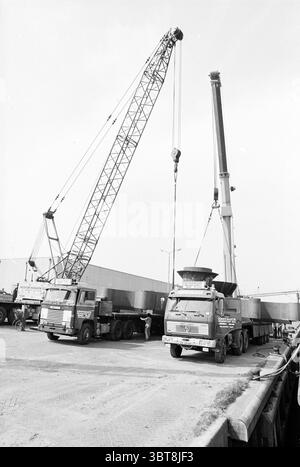 Hebearbeiten Fa Genius IJmuiden Lifting Work Ships IJmuiden the Netherlands, Whizgle News, Dutch Desk, Niederlande, 1950 - 2000 am 11-04-1981. Das Bild enthält diese Themen. Die Szene zeigt zwei große Kräne, die über einer Baustelle thronen. Ein Kran ist besonders hoch und schlank, mit einem langen Arm nach oben, während der andere kürzer, aber stabiler ist und ein robustes Design bietet. Beide Kräne befinden sich in der Nähe großer Lkw, die parallel zueinander auf einer gepflasterten Fläche abgestellt werden. Bei den Lkw handelt es sich um Schwerlastfahrzeuge, die sich durch ihre sperrigen Rahmen und das industrielle Design auszeichnen. Stockfoto