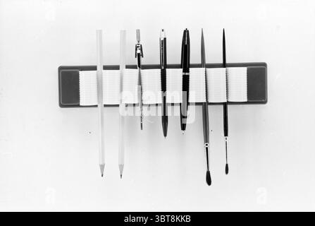 Invention Mr. Duynstee Inventions, Whizgle News, Dutch Desk, Niederlande, 1950 - 2000 am 26-07-1967. Das Bild enthält diese Themen. Die Szene besteht aus einer Anordnung von Objekten in einem minimalistischen Stil, die eine monochromatische Ästhetik betont. In der Mitte befindet sich eine rechteckige Plattform für eine Reihe von Schreibgeräten, die in einer geraden Reihe ausgerichtet sind. Auf der linken Seite weisen zwei Bleistifte, einer etwas länger als der andere, einen weichen, hellen Farbton auf, der sich von den dunkleren Tönen der übrigen Kollektion abhebt. Daneben zeigt ein schmaler Pinsel feine Borsten, die auf beide Kunstwerke hinweisen Stockfoto