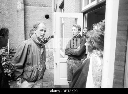 Marinekrankenhaus besetzte, Whizgle News, Dutch Desk, Niederlande, 1950 - 2000 am 14-09-1991. Diese Themen sind in der Abbildung dargestellt. In der Szene versammelt sich eine Gruppe von Personen vor einer teilweise offenen Tür, die in ein Gebäude führt. Die Architektur ist klassisch gemauert und weist auf eine Mischung aus historischem Charme und moderner Funktionalität hin. Die Ziegel haben einen gedämpften Ton, der der Umgebung eine erdige Atmosphäre verleiht. Im Vordergrund steht ein Mann mit einem ernsten Ausdruck, der anscheinend im Gespräch ist. Er trägt eine lässige Jacke, und sein konzentriertes Auftreten vermittelt ein Gefühl von Autorität Stockfoto
