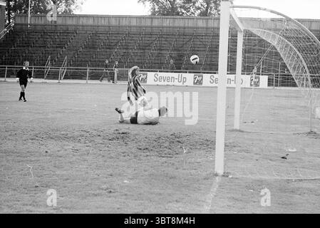 Fußballspiel RCH - ? Heemstede the Netherlands, Whizgle News, Dutch Desk, Niederlande, 1950 - 2000 auf 30-09-1973. Dies sind die Themen im Bild. Die Szene fängt einen dynamischen Moment auf einem Fußballfeld ein, voller Energie und Spannung. Im Vordergrund befindet sich ein Spieler mit einem gestreiften Trikot mitten in der Luft, nachdem er gerade den Ball in Richtung Tor geschlagen hat. Sein Ausdruck vermittelt eine Mischung aus Entschlossenheit und Begeisterung, was die Bedeutung des Augenblicks andeutet. Der Torhüter in kontrastierender Uniform wird auf dem Boden positioniert, nachdem er im letzten Graben versucht hat, den Schuss zu blockieren. Sein Stockfoto