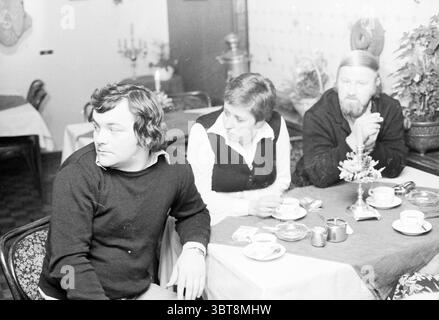 Verschiedene Leute unterhalten sich in einer Gastronomie, Whizgle News, Dutch Desk, Niederlande, 1950 - 2000 am 05-1979. Dies sind die Themen im Bild. In einem gemütlichen Innenbereich sitzen drei Personen um einen Tisch mit einer weißen Tischdecke. Das Arrangement umfasst mehrere kleine Tassen, wahrscheinlich für Kaffee oder Tee, und ein paar Utensilien, die ordentlich daneben liegen. Die erste Person, die sich links befindet, hat mittellange dunkle Haare und trägt einen schwarzen Pullover. Er blickt von der Kamera weg und strahlt ein nachdenkliches oder kontemplatives Verhalten aus. Neben ihm sitzt eine Frau mit kurzen Haaren. Stockfoto