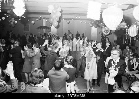 Partyabend Nutsspaarbank Parties Nuts united Savings Banks, Whizgle News, Dutch Desk, Niederlande, 1950 - 2000 am 02-12-1967. Das Bild enthält diese Themen. Die Szene ist lebendig und voller Feiern. Die Komposition fängt ein lebhaftes Treffen mit verschiedenen Gruppen von Menschen ein, die sich mit Tanz und Unterhaltung beschäftigen. Die Menge ist in einer Reihe formeller Kleidung gekleidet, darunter Anzüge und elegante Kleider, die eine Mischung aus klassischen Stilen und Farben bieten. Bunte Ballons schweben über den Teilnehmern und schaffen eine festliche Atmosphäre. Die Laternen hängen von der Decke und geben ein warmes Licht Stockfoto