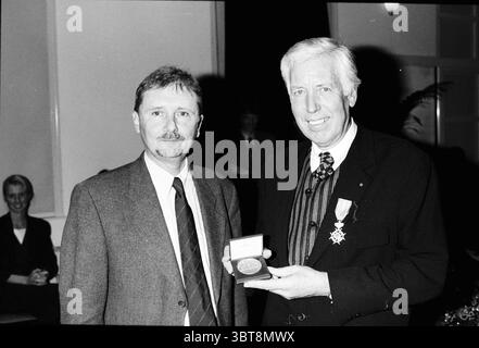 Ehrenmedaille Herr van Diepen Zaandam, Whizgle News, Dutch Desk, Niederlande, 1950 - 2000 am 19.12.1995. Dies sind die Elemente im Bild. Die Szene zeigt zwei Männer, die in einem formellen Rahmen nebeneinander stehen, wahrscheinlich während einer Zeremonie oder einer Preisverleihung. Der erste Mann links hat ein leichtes Lächeln und trägt einen Anzug mit Krawatte, der ein selbstbewusstes Verhalten ausstrahlt. Sein Haar ist ordentlich gestylt, und er scheint im Moment beschäftigt zu sein. Auf der rechten Seite hält der zweite Mann eine Medaille oder Auszeichnung hoch und zeigt sie stolz vor dem Publikum. Er trägt auch ein formelles Outfit, das in Stockfoto