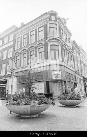Außenansicht des extra Neerlandia Building, Whizgle News, Dutch Desk, Niederlande, 1950 - 2000 am 16-02-1972. Dies sind die Elemente im Bild. Die Szene zeigt ein Eckgebäude mit einem unverwechselbaren architektonischen Stil, gekennzeichnet durch hohe, schmale Fenster und dekorative Elemente, die auf eine historische Bedeutung hinweisen. Die Fassade besteht hauptsächlich aus dunklem Ziegelstein und steht im Kontrast zu den leichteren, strukturierten Materialien des unteren Abschnitts, der aus Holz aussieht und im Laufe der Zeit verändert wurde. Im Vordergrund befinden sich große Beton-Pflanzgefäße, die wie flache Schüsseln geformt sind, die vielleicht eine Mischung aus Grün enthalten Stockfoto