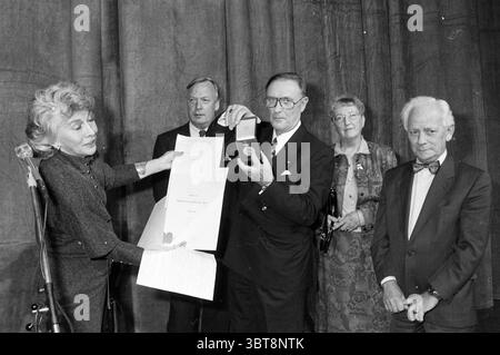 Ehrenmedaille Alberdingk Thijm Theaterverein H'kerk Heemskerk, Whizgle News, Dutch Desk, Niederlande, 1950 - 2000 am 10.11.1991. Diese Themen werden in der Abbildung angezeigt. Die Szene zeigt ein formelles Ereignis, möglicherweise eine Preisverleihung, die durch ein Gefühl der Feier und Anerkennung gekennzeichnet ist. Im Vordergrund steht links eine Frau, deren schulterlanges Haar elegant gestylt ist. Sie trägt ein dunkles Outfit und präsentiert mit der einen Hand ein Dokument, während sie in der anderen eine Auszeichnung hält. Ihr Ausdruck vermittelt Ernsthaftigkeit und Stolz, was die Wichtigkeit des Augenblicks andeutet. Stockfoto