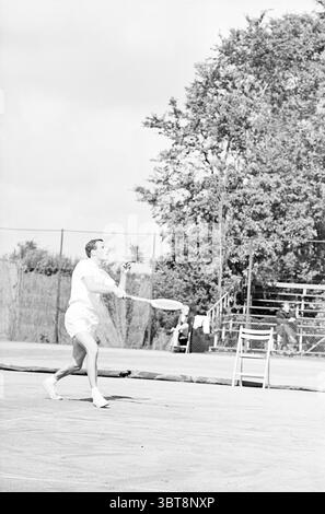 Tennis Brederode III Jaidip Mukerjea-Tom Okker Santpoort, Whizgle News, Dutch Desk, Niederlande, 1950 - 2000 auf 30-07-1965. Das Bild enthält diese Themen. Die Szene zeigt einen lebhaften Tennisplatz voller Energie und Bewegung. Im Vordergrund wird ein Spieler mitten im Schwung erfasst und zeigt einen entschlossenen Ausdruck, während er sich auf den Ball vorbereitet. Die Kleidung spiegelt einen klassischen, sportlichen Look mit einem Kurzarm-Shirt und Shorts wider und unterstreicht die sportliche Essenz des Augenblicks. Um den Spieler herum befindet sich ein weitläufiger Platz mit einer strukturierten Oberfläche, die auf die jüngsten Aktivitäten hinweist. Die Kulisse Stockfoto