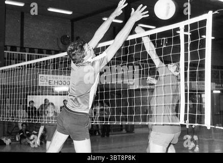 Volleyballturnier VNU Amsterdam VNU Verband niederländischer Verleger Volleyball Amsterdam Niederlande, Whizgle News, Dutch Desk, Niederlande, 1950 - 2000 am 15.06.1985. Die Abbildung zeigt diese Themen. In einem Gymnasium mit lebhafter Atmosphäre spielen zwei Athleten ein intensives Volleyballspiel. Die Spieler sind mitten in der Action, wobei der eine mit ausgestreckten Armen hoch reicht, um einen Volley zu blockieren, der auf ihre Netzseite gerichtet ist, während der andere sich in der Mitte des Sprunges auf den Ball vorbereitet. Ihre Ausdrücke vermitteln Entschlossenheit und Konzentration. Die Spieler tragen sportliche Shorts und taillierte Oberteile, die sich in Kontrastfarbe befinden Stockfoto