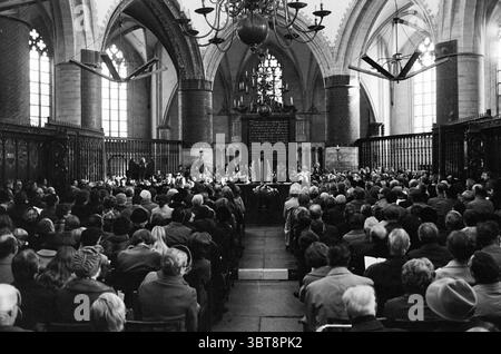 Heilige Messe Grote Kerk Grote Kerk Haarlem Kirchen St. Bavokerk, Whizgle News, Dutch Desk, Niederlande, 1950 - 2000 am 05-11-1971. Die Abbildung zeigt diese Themen. Die Szene fängt eine große Versammlung in einem großen, historischen Gebäude ein, das von hoch aufragenden gotischen Bögen charakterisiert ist, die zu einer gewölbten Decke hinaufragen. Die Architektur besteht aus komplizierten Steinarbeiten, wobei das Licht durch hohe, enge Buntglasfenster gefiltert wird, die bunte Muster auf den Steinboden werfen. Im Vordergrund sitzt eine bunte Menschenmenge in ordentlichen Reihen, die alle auf einen zentralen Blickpunkt gerichtet sind Stockfoto