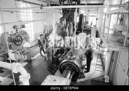 Wiedereröffnung der Dampfpumpenstation auf halbem Wege Öffnungen Inbetriebnahme Dampfpumpenstation und Dampfpumpenstation Halfweg, Whizgle News, Dutch Desk, Niederlande, 1950 - 2000 am 01-04-1989. Die Abbildung zeigt diese Themen. Die Szene zeigt eine industrielle Umgebung, die durch eine Mischung aus Maschinen und menschlicher Aktivität gekennzeichnet ist. Der Innenraum ist geräumig, mit hohen Decken und großen Fenstern, die natürliches Licht hereinlassen und den Arbeitsbereich mit einem weichen, diffusen Licht beleuchten. Verschiedene mechanische Komponenten dominieren den Raum, darunter große, zylindrische Maschinen mit Gleaming Me Stockfoto