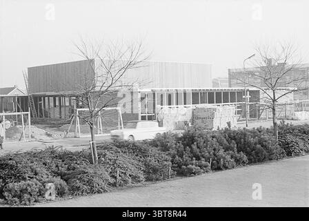 Zusätzliches Clubgebäude Rijsenhout Exterior, Whizgle News, Dutch Desk, Niederlande, 1950 - 2000 am 19.12.1968. Diese Themen sind in der Abbildung dargestellt. Die Szene zeigt eine Baustelle mit einer teilweise gebauten Struktur, die den Vordergrund dominiert. Das Gebäude hat ein modernes Design, das durch eine Kombination aus Holzlatten und großen Glaspaneelen gekennzeichnet ist, die eine luftige, zeitgenössische Ästhetik vermitteln. Es scheint eine einstöckige Struktur zu sein, und der Rahmen weist auf bedeutende Fortschritte in Bereichen hin, die noch exponiert sind. Um das Gebäude herum befinden sich mehrere Stapel von Baumaterialien, einschließlich Stockfoto