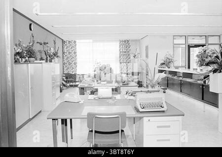 Int. AmroBank Zwanenburg Interior, Whizgle News, Dutch Desk, Niederlande, 1950 - 2000 am 13-09-1971. Dies sind die Themen im Bild. Die Szene zeigt eine geräumige Büroumgebung, die sich durch ein klares, organisiertes Layout auszeichnet. Es gibt mehrere in einem Raster angeordnete Arbeitsplätze, die jeweils mit einem einfachen Schreibtisch und einem ergonomischen Stuhl ausgestattet sind. Die Schreibtische sind mit Retro-Schreibmaschinen verziert, die neben minimalen dekorativen Elementen wie Topfpflanzen einen Schwerpunkt auf schriftlicher Kommunikation legen. Die Farbpalette ist monochromatisch, dominiert von Grautönen, die einen klassischen und etwas Au betonen Stockfoto