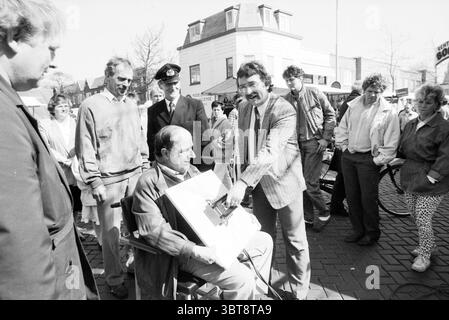 Inbetriebnahme des Strommarktes Florisstraat Inbetriebnahme Haarlem Floresstraat, Whizgle News, Dutch Desk, Niederlande, 1950 - 2000 am 30-03-1989. Dies sind die Themen im Bild. Eine lebhafte Straßenszene entfaltet sich, in der sich eine Gruppe von Individuen um eine zentrale Figur versammelt. Im Vordergrund bewegt sich ein Mann in einem Anzug animiert und zieht die Aufmerksamkeit der Zuschauer auf sich. Er zeigt ein breites Lächeln und strahlt Begeisterung aus, während er ein faszinierendes Objekt präsentiert, das auf ein Element der Überraschung oder Unterhaltung hinweist. An seiner Seite erscheint ein sitzender Mann mit kurzen Haaren verwickelt Stockfoto