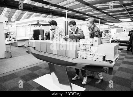 Europort 1989 in RAI in Amsterdam Visserij et al. Fishmongers Fishing Amsterdam Niederlande, Whizgle News, Dutch Desk, Niederlande, 1950 - 2000 am 14-11-1989. Dies sind die Themen im Bild. In einem großzügigen Ausstellungsbereich stellen drei junge Menschen ein großes, detailliertes Modell eines Frachtschiffes vor. Das Modell, das auf einem schlanken Ständer montiert ist, besticht durch sein kompliziertes Design, das zahlreiche Container auf dem Deck des Schiffes zeigt. Die Umgebung ist hell und luftig, geprägt von Oberlichtern, die natürliches Licht einströmen lassen und eine lebendige Atmosphäre schaffen. Stockfoto