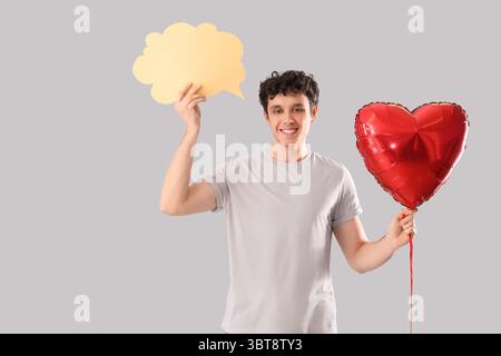 Hübscher junger glücklicher Mann mit Herzballon und Sprechblase auf grauem Hintergrund Stockfoto