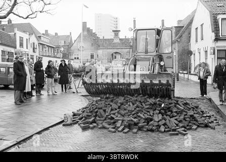 Renovierung des Gasthuisplein Zandvoort durch Bürgermeister Zandvoort Zandvoort Gasthuisplein, Whizgle News, Dutch Desk, Niederlande, 1950 - 2000 am 06-02-1984. Dies sind die Elemente im Bild. Die Szene präsentiert ein geschäftiges urbanes Ambiente, das anscheinend einer Art von Bau- oder Renovierungsarbeiten unterzogen wird. Im Mittelpunkt der Komposition steht ein großes, schweres Baufahrzeug, dessen Schaufel mit dunklen, ungleichmäßig gestapelten Ziegeln gefüllt ist. Das Fahrzeug steht in starkem Kontrast zur Umgebung und zeigt seinen industriellen Charakter in einem eher traditionellen urbanen Hintergrund. Die Straße unter dem Fahrzeug i Stockfoto
