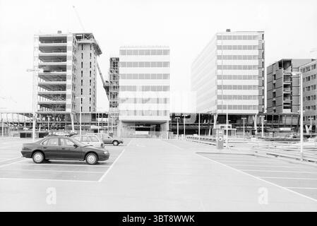 New Construction World Trade, Whizgle News, Dutch Desk, Niederlande, 1950 - 2000 am 01-10-1995. Dies sind die Elemente im Bild. Die Szene zeigt eine krasse urbane Landschaft mit zwei großen, modernen Gebäuden, die das Zentrum dominieren. Diese Strukturen zeichnen sich durch ihre charakteristischen rechteckigen Formen und eine Reihe von großen Fenstern aus, die ein elegantes architektonisches Design bieten. Die Gebäude auf der linken Seite befinden sich noch im Bau, was an freiliegenden Stahlträgern und Gerüsten zu erkennen ist, was auf laufende Arbeiten hindeutet. Im Vordergrund erstreckt sich ein großer Parkplatz mit mehreren geparkten Fahrzeugen Stockfoto