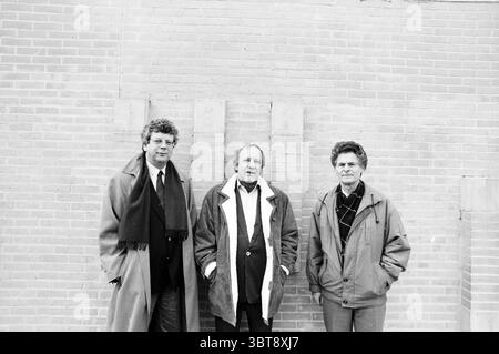 Management of Scaia Wines Lisse, Whizgle News, Dutch Desk, Niederlande, 1950 - 2000 am 27-01-1991. Das Bild enthält diese Themen. Die Szene zeigt drei Personen, die zusammen vor einer strukturierten Ziegelwand stehen. Die Wand besteht aus warmen, erdroten Tönen, was ihr ein rustikales Ambiente verleiht. Links trägt ein Mann mit lockigen Haaren einen dunklen Mantel und einen Schal, der ein poliertes und formelles Aussehen ausstrahlt. Seine Haltung ist selbstbewusst, mit einem leichten Lächeln, das auf ein warmes Verhalten hindeutet. Stockfoto