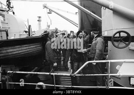 Rettungsdienst der Rettungsbrigade, Whizgle News, Dutch Desk, Niederlande, 1950 - 2000 am 15-01-1974. Das Bild enthält diese Themen. In einer belebten maritimen Umgebung steht eine Gruppe rauer Individuen auf einem Deck, die in einem Moment der Kameradschaft verwickelt sind. Die Szene ist durchdrungen von einem grauen, bewölkten Ambiente, mit weichem, gedämpftem Licht, das durch die Wolken filtert und eine etwas düstere, aber intime Stimmung erzeugt. Die Männer sind in schweren, verwitterten Mänteln gekleidet, die auf die Elemente hinweisen, denen sie häufig auf See begegnen. Ihre Gesichtsausdrücke reichen von ernst bis freundlich, mit ein paar s Stockfoto