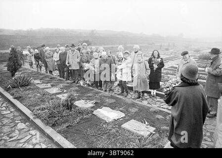 Parool Group Honorary Cemetery Honorary Cemetery Overveen, Whizgle News, Dutch Desk, Niederlande, 1950 - 2000 am 04-02-1987. Dies sind die Themen im Bild. In einer düsteren Szene steht eine Gruppe von Menschen in einer Reihe, positioniert auf einem Friedhof, der eine gedämpfte Atmosphäre ausstrahlt. Die Kulisse wirkt bedeckt, mit einer Nebeldecke, die einen grauen Farbton über alles wirft, was das Gefühl der Festlichkeit verstärkt. Die Figuren tragen schwere Mäntel und Hüte, die für kälteres Wetter typisch sind, und zeigen eine Reihe von Emotionen, viele mit herabgesetzten Augen oder besinnlichen Ausdrücken. Einige Personen Stockfoto