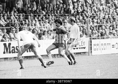 Haarlem - PSV Football Haarlem, Whizgle News, Dutch Desk, Niederlande, 1950 - 2000 am 15-05-1977. Das Bild enthält diese Themen. Die Szene zeigt einen dynamischen Moment auf einem Fußballfeld, mit vibrierender Energie von den Spielern und der Menge. Im Vordergrund sind zwei Athleten voll in die Action eingebunden. Ein Spieler, der ein hellrotes Trikot mit kontrastierenden weißen Streifen trägt, scheint den Ball geschickt zu manövrieren, während der gegnerische Spieler in weiß versucht, abzufangen. Das Gras darunter ist üppig grün, gepflegt und frisch geschnitten, was eine lebendige Kulisse für Sie bietet Stockfoto