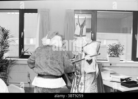 Sinterklaas on Haarlems Dagblad Haarlem the Netherlands, Whizgle News, Dutch Desk, Niederlande, 1950 - 2000 am 28-11-1995. Das Bild enthält diese Themen. In einem hellen Innenraum des Büros interagieren zwei Figuren. Eine Figur trägt ein traditionelles Weihnachtsmannskostüm, komplett mit einem flauschigen roten Mantel und einer Hose, mit weißem Besatz und einem passenden roten Hut. Die zweite Figur verkörpert ein königliches Aussehen, verziert mit kunstvollen weiß-goldenen Gewändern. Diese Figur trägt auch einen hohen, reich verzierten Gehrenhut und hält einen Stab, was auf eine Rolle der Autorität oder des Wohlwollens hindeutet. Die setti Stockfoto