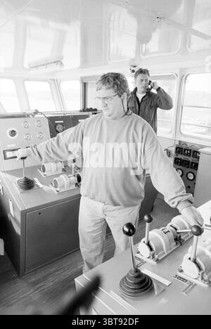 Bagger-Hafen von IJmuiden IJmuiden the Netherlands, Whizgle News, Dutch Desk, Niederlande, 1950 - 2000 am 02-04-1997. Diese Themen sind in der Abbildung dargestellt. Die Szene fängt einen dynamischen Moment an Bord eines Schiffes ein, mit zwei Männern im Fokus. Im Vordergrund steht ein Mann, der tief in die Steuerung des Schiffs eingreift. Er trägt ein locker geschnittenes, helles Sweatshirt, und sein Ausdruck spiegelt Konzentration wider, während er die Hebel und Zifferblätter vor ihm anfasst. Die Brille des Mannes verleiht seinem Aussehen einen akademischen Touch und deutet auf Erfahrung hin. Im Gegensatz dazu ist der zweite Mann leicht positioniert Stockfoto